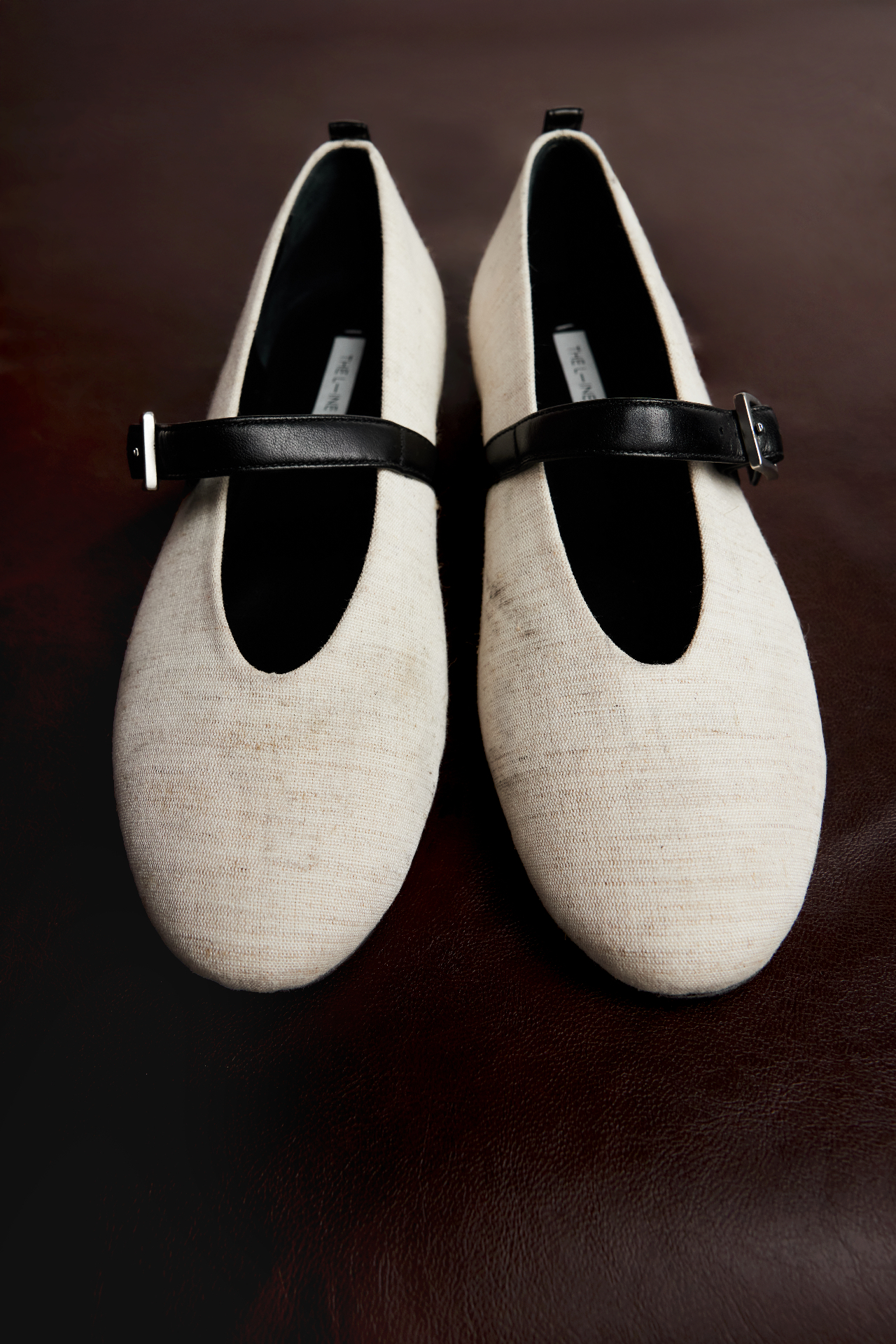 Cream linen mary jane flats with black leather strap on dark background
