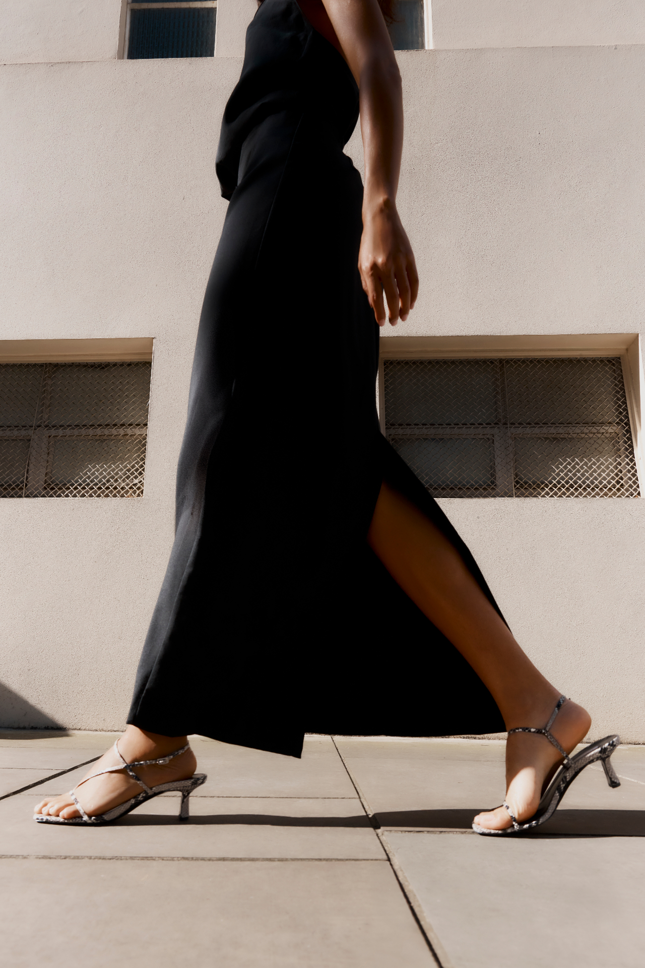Model walking in a black dress with snakeskin heeled sandals